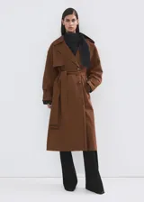 Chaqueta larga tipo trench color marrón, con diseño recto, solapas anchas, doble botonadura, bolsillos laterales y cinturón desmontable de la misma tela.