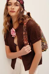 Cardigan de punto metalizado color marrón, de manga corta y diseño abierto al frente con cierre de botón único y detalle de flor aplicada.
