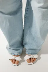 Sandalia de tacón fino color blanco, con tira delantera ancha con detalle de lazo y terminación en punta redonda.