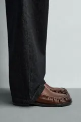 Mocasín de vestir color marrón oscuro, fabricado en piel lisa, con detalle de antifaz en el empeine y costura visible en la puntera. Presenta una horma cuadrada y suela con ligero tacón.