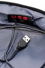 Mochila urbana con carcasa frontal rígida de color negro con diseño geométrico y logo 'VM' en blanco. Los laterales y la espalda son de tela gris jaspeada. Incluye un candado de combinación de tres dígitos integrado en el lateral.