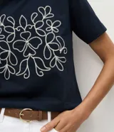 Remera de algodón color azul marino, con cuello redondo, mangas cortas y un bordado frontal en color blanco con diseño simétrico de motivos florales.