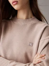Sweater color beige de punto de algodón orgánico, con cuello redondo alto, mangas largas y logo bordado en el pecho.