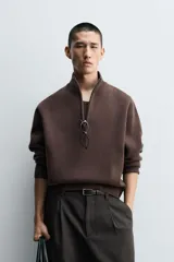 Jersey de punto de corte regular, color gris oscuro, con cuello subido y cierre frontal de cremallera. Presenta mangas largas y acabados en rib en puños y ruedo.