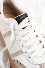 Zapatillas bajas de cuero color blanco y beige, con suela gruesa marrón y cordones blancos.