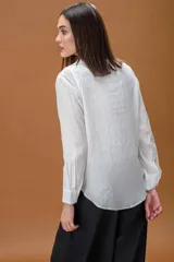 Camisa blanca de corte clásico con cuello camisero, manga larga y bolsillo frontal, que incluye una musculosa interior con detalle de encaje visible en el escote.