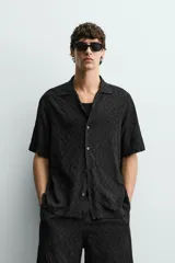 Camisa de corte relajado con cuello bowling y manga corta. Confeccionada en tejido fluido con textura jacquard de patrón geométrico y cierre frontal de botones.