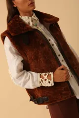 Chaleco de piel sintética en color chocolate, con cierre frontal y detalles de cuero en los bordes. Presenta un diseño de cuello solapa y ajuste lateral con hebillas.