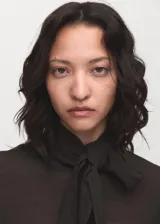 Blusa de color marrón oscuro con textura, cuello alto envolvente con detalle de fular integrado, manga larga con puños abotonados y diseño recto.