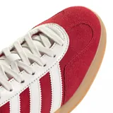 Championes adidas Gazelle Indoor, confeccionados en gamuza color rojo con las icónicas tres tiras laterales y refuerzo en el talón en color blanco. Presenta suela de goma color caramelo y el nombre del modelo en letras doradas en el lateral.
