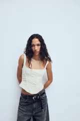 Top estilo corset de color blanco con escote cuadrado y tirantes anchos. Presenta paneles laterales y centrales con tejido drapeado, estructura entallada y cierre posterior con cremallera.