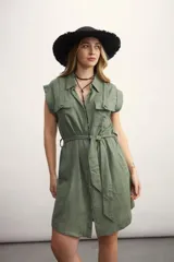 Vestido camisero corto color beige, con cuello clásico, mangas cortas con puños, dos bolsillos con solapa en el pecho, cinturón de lazo y cierre frontal con botones.