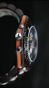 Reloj cronógrafo de la colección Imperial, con caja de madera de ébano oscuro y bisel técnico. La esfera negra presenta subdiales con textura de madera natural, indicador de fase lunar y fechador. La malla combina eslabones de acero inoxidable pulido con madera de ébano, ofreciendo un diseño sofisticado y resistente.