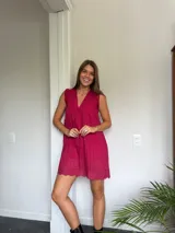 Vestido corto color fucsia, con escote en V profundo y mangas cortas tipo volado. Presenta un diseño con textura de bordado inglés o perforado y un corte imperio con frunce que da volumen a la falda.