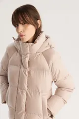 Campera puffer corta color beige con capucha desmontable, cierre frontal con cremallera y botones a presión, y cordón ajustable en el ruedo. Diseño acolchado con bolsillos laterales.
