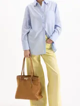 Bolso tipo tote color gris, confeccionado en cuero vacuno, con asas largas para hombro, detalles metálicos personalizados, cierre central y llavero con candado y llave colgante.