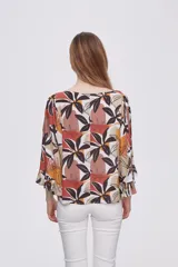Blusa estampada con flores en tonos marrones, naranjas y negros, con mangas 3/4 acampanadas y cuello redondo.