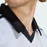 Camiseta deportiva Adidas de manga corta, color celeste con sutiles rayas verticales, cuello polo negro en V y las clásicas tres tiras negras en los hombros. Cuenta con el logotipo de la marca y la inscripción "adidas" en el pecho en color negro.