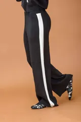 Conjunto de dos piezas compuesto por un buzo tipo hoodie con cierre frontal, capucha y bolsillos laterales, y un pantalón de corte recto. Ambas prendas son de color negro con detalles de bandas laterales en blanco.