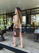 Bolso matera de cuero color marrón con doble asa de mano y correa larga desmontable. Incluye accesorio decorativo de borlas rosas y blancas.