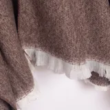 Ruana color marrón con tejido de espiga y flecos blancos en el borde inferior.