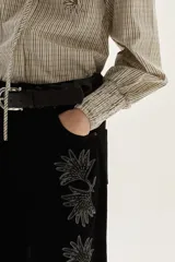 Blusa de algodón con estampado de rayas verticales en tonos crudo y negro. Presenta cuello mao con lazo para atar, bordados florales en negro y beige en la zona del pecho y hombros, y mangas largas con puños fruncidos elásticos.