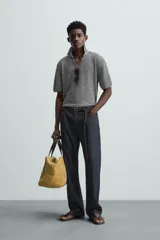 Polo de punto de manga corta con cuello solapa y abertura frontal en forma de V. Presenta un patrón de rayas horizontales finas en blanco y negro, con un acabado texturizado y un calce relajado.