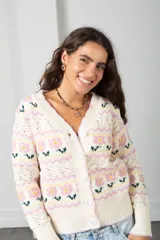 Cárdigan de punto color crema con diseño de flores en tonos rosados y verdes, guardas caladas, escote en V, cierre frontal con botones y terminaciones acanaladas.