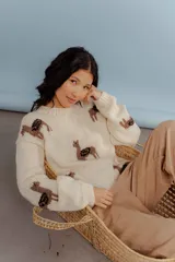 Buzo de lana merino color crema, con diseño tejido de llamas en tonos marrones. Presenta cuello redondo, mangas largas con hombros caídos y puños acanalados.