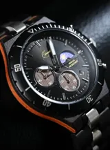 Reloj cronógrafo de la colección Imperial, con caja de madera de ébano oscuro y bisel técnico. La esfera negra presenta subdiales con textura de madera natural, indicador de fase lunar y fechador. La malla combina eslabones de acero inoxidable pulido con madera de ébano, ofreciendo un diseño sofisticado y resistente.