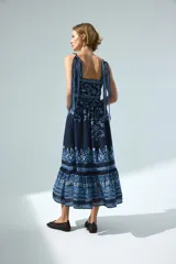 Vestido midi de algodón azul marino con estampado floral y geométrico en tonos celestes y blancos. Presenta escote recto, breteles ajustables con moñas, cuerpo entallado y falda acampanada con volados fruncidos en la parte inferior.