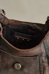 Cartera mini de cuero marrón con terminación gastada, cuerpo blando, bolsillos exteriores y solapa con cierre de hebilla. Incluye herrajes metálicos envejecidos y detalles colgantes con candado y llave.