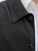 Campera tipo trench liviana de corte recto y largo medio, color negro, con cuello camisero, cierre frontal de botones y puños ajustables con trabilla.