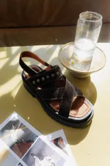 Sandalias de gamuza marrón con diseño de tiras cruzadas en el empeine, decoradas con tachas metálicas. Posee una suela de plataforma dentada de color negro y plantilla de cuero en tono natural.