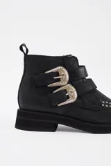 Botín de cuero vacuno color marrón, con punta fina y detalle de tachas metálicas en la parte superior. Presenta una suela de plataforma plana de color negro.