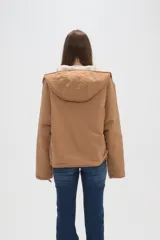 Campera de poliéster color tostado con capucha, cierre frontal con botones a presión y bolsillos delanteros amplios. El interior está forrado con corderito para mayor abrigo.