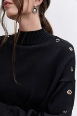 Sweater de punto negro con cuello alto y detalle de ojalillos metálicos a lo largo de las mangas. Presenta un corte holgado con puños y ruedo acanalados.