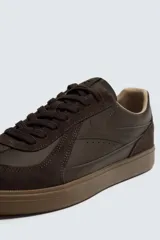 Zapatilla deportiva de estilo retro con diseño de paneles combinados en tonos beige y crema. Presenta detalles en gamuza y una suela de goma en color caramelo.