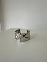 Brazalete rígido de acero quirúrgico con diseño de superficie irregular y efecto ondulado, acabado brillante.