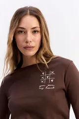 Remera de manga larga color marrón, con cuello redondo y estampa sutil en el pecho con diseño de juego de ta-te-ti y texto.