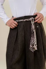 Pantalón wide leg de tiro alto en color negro, con diseño de pinzas delanteras que aportan volumen y caída fluida. Incluye bolsillos laterales y un lazo desmontable en la cintura que combina cordón con cinta de estampado animal print.