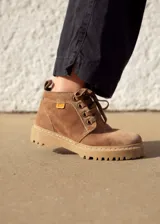 Bota acordonada de cuero color arena, con interior forrado en tela escocesa roja y negra, y suela de goma color caramelo.