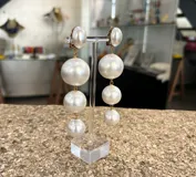 Aros colgantes largos con clip, formados por tres perlas blancas de tamaño decreciente unidas por eslabones dorados.