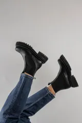 Botas tipo chelsea de cuero negro con textura granulada, paneles laterales elásticos y suela track robusta de goma.