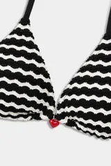 Top de bikini tipo triángulo de tirantes finos negros, con patrón de ondas blancas y negras en relieve. Presenta un pequeño dije en forma de corazón en el centro.