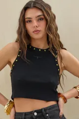 Musculosa crop de morley negro con cuello redondo, decorada con tachas en forma de estrella doradas a lo largo del cuello y sisas. Cuenta con un pequeño bordado frontal en el centro del pecho.