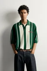 Polo de punto boxy fit color verde oscuro y blanco, de manga corta, con cuello solapa, cierre frontal con botones y detalle de texto bordado a contraste en el pecho.