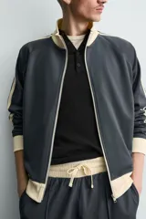 Sudadera de corte relajado en color azul marino con cuello alto y cierre frontal de cremallera. Presenta bandas laterales en color crema a contraste que recorren las mangas, puños y bajo en tejido rib, y bolsillos laterales de vivo.