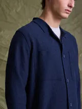 Overshirt de tejido de punto color azul marino, con cuello camisero, cierre frontal de botones y dos bolsillos frontales tipo parche.