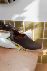 Zapatos tipo mocasín de cuero color marrón oscuro, con diseño de textura lisa en la parte delantera y textura de reptil en el talón. Cuentan con cierre trasero y suela plana de color claro.
